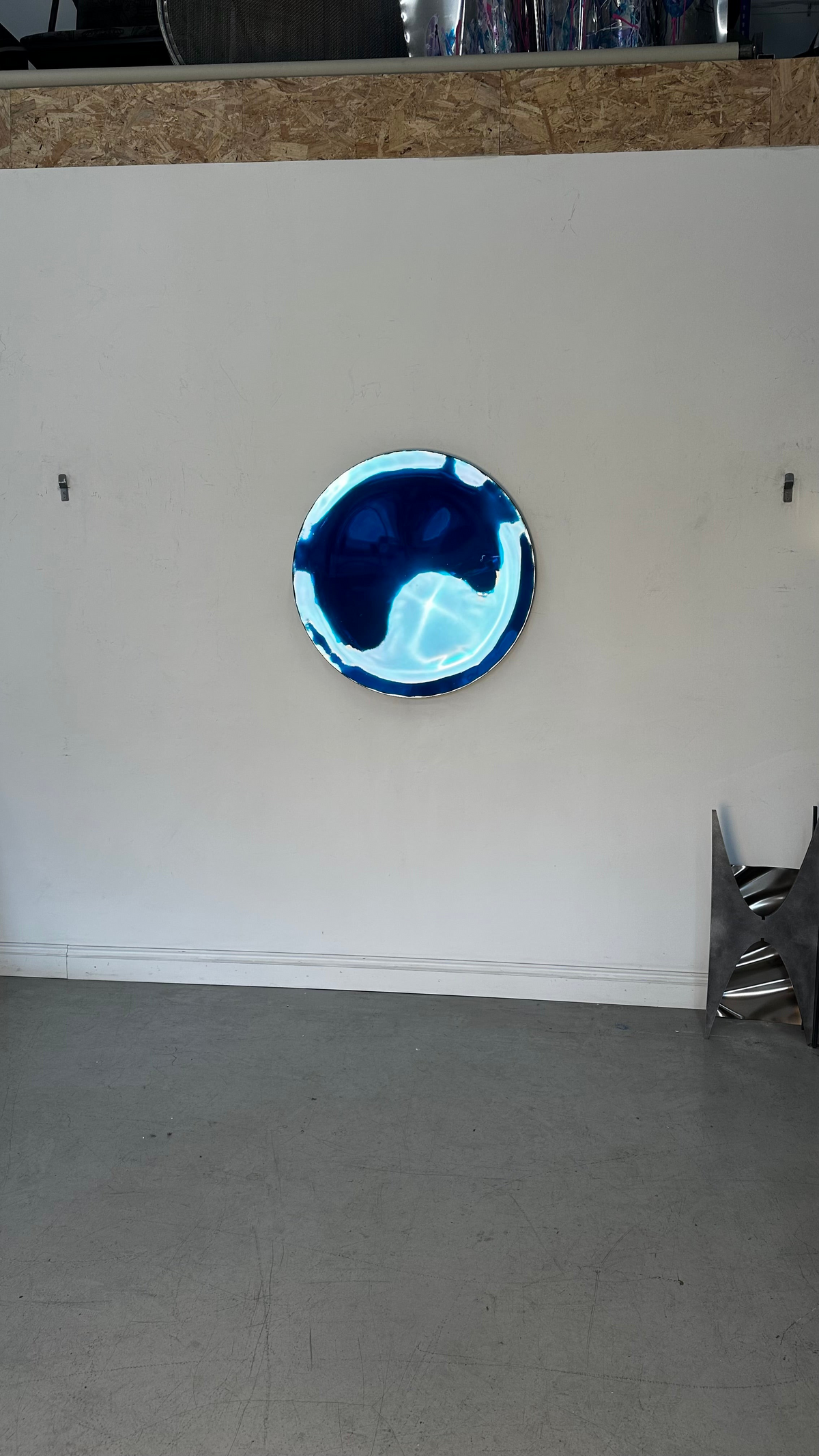 Piers Henry Interiors blue metal concave wall mirror with a polished, fluid surface creating dynamic light reflections.
