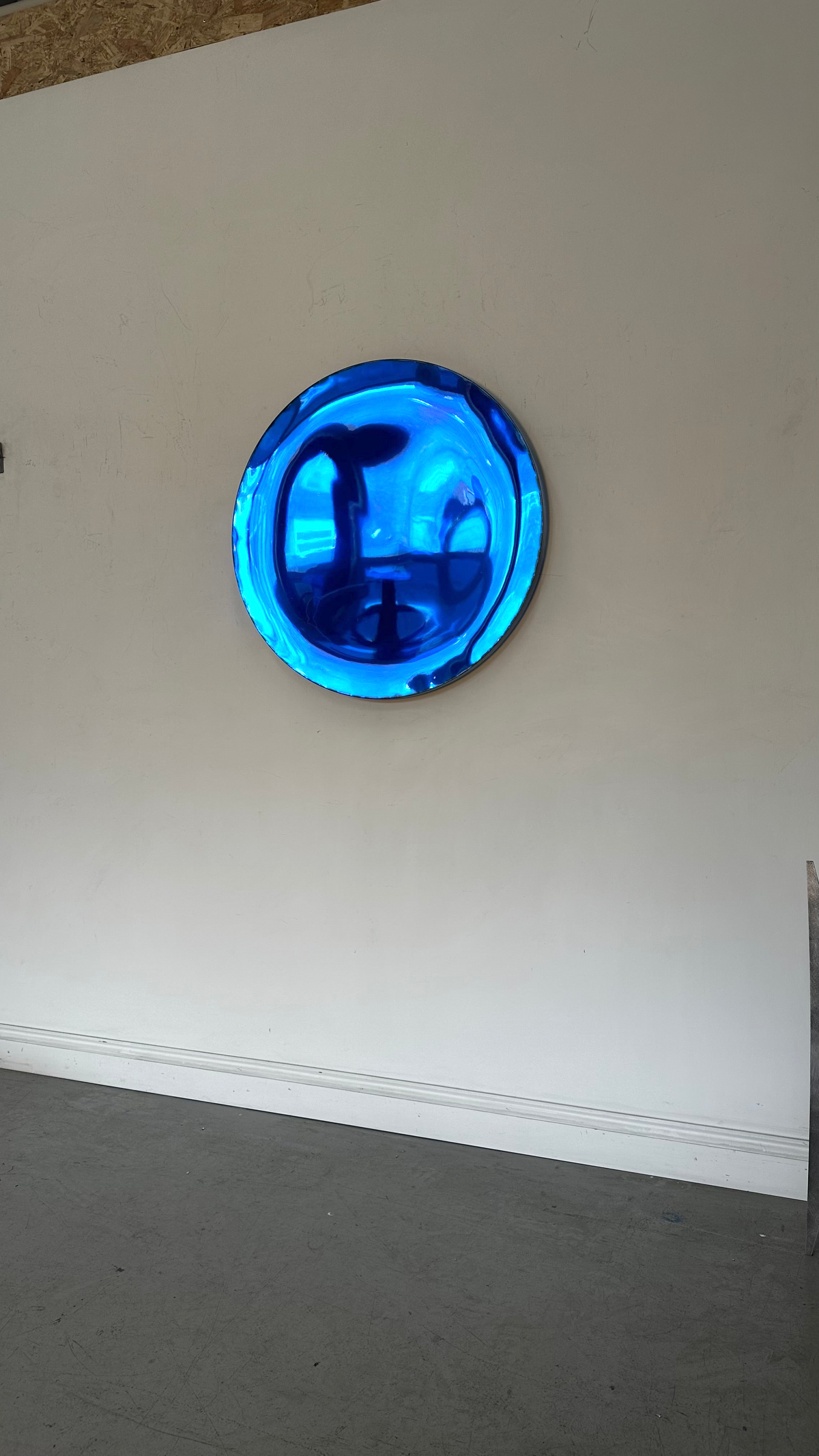 Piers Henry Interiors blue concave metal wall mirror with a polished, sculptural curved surface on a white wall.